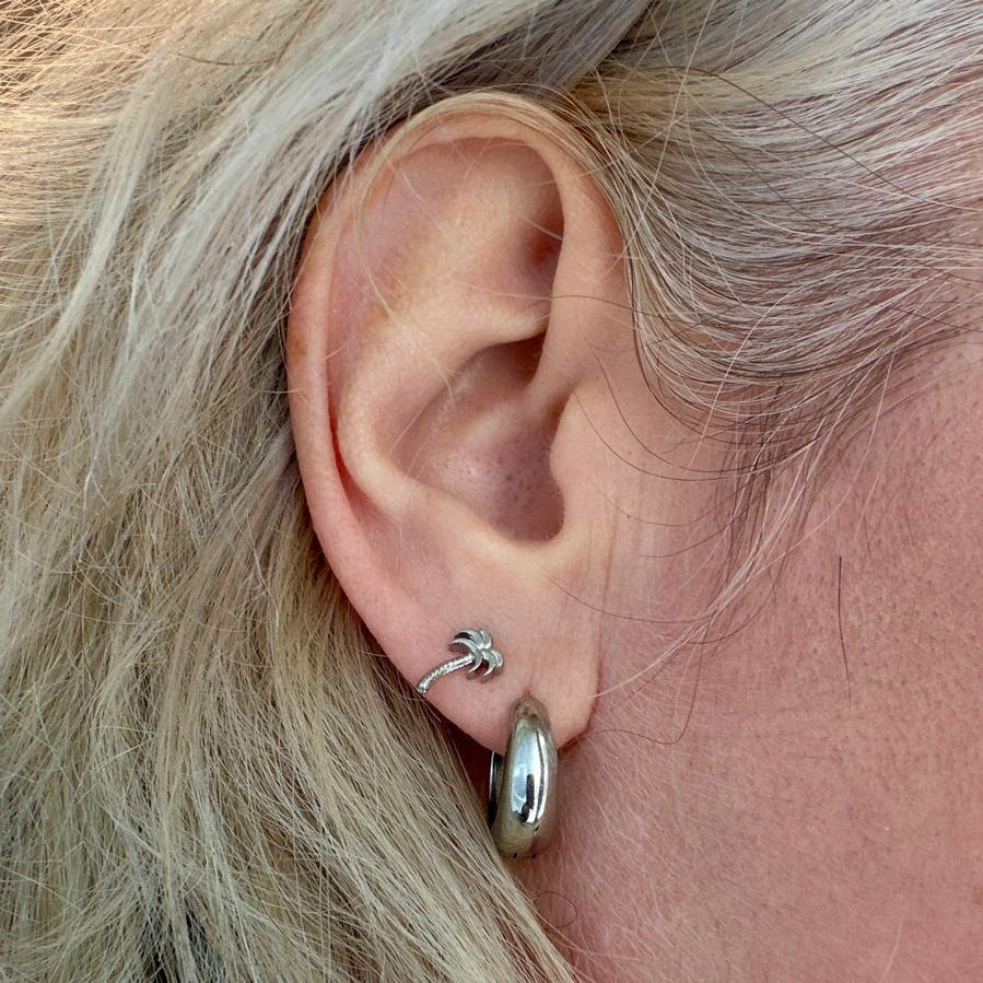 Een oor met daarin twee oorbellen. Een zilveren ring oorbel en een oorsteker in de vorm van een palmboom